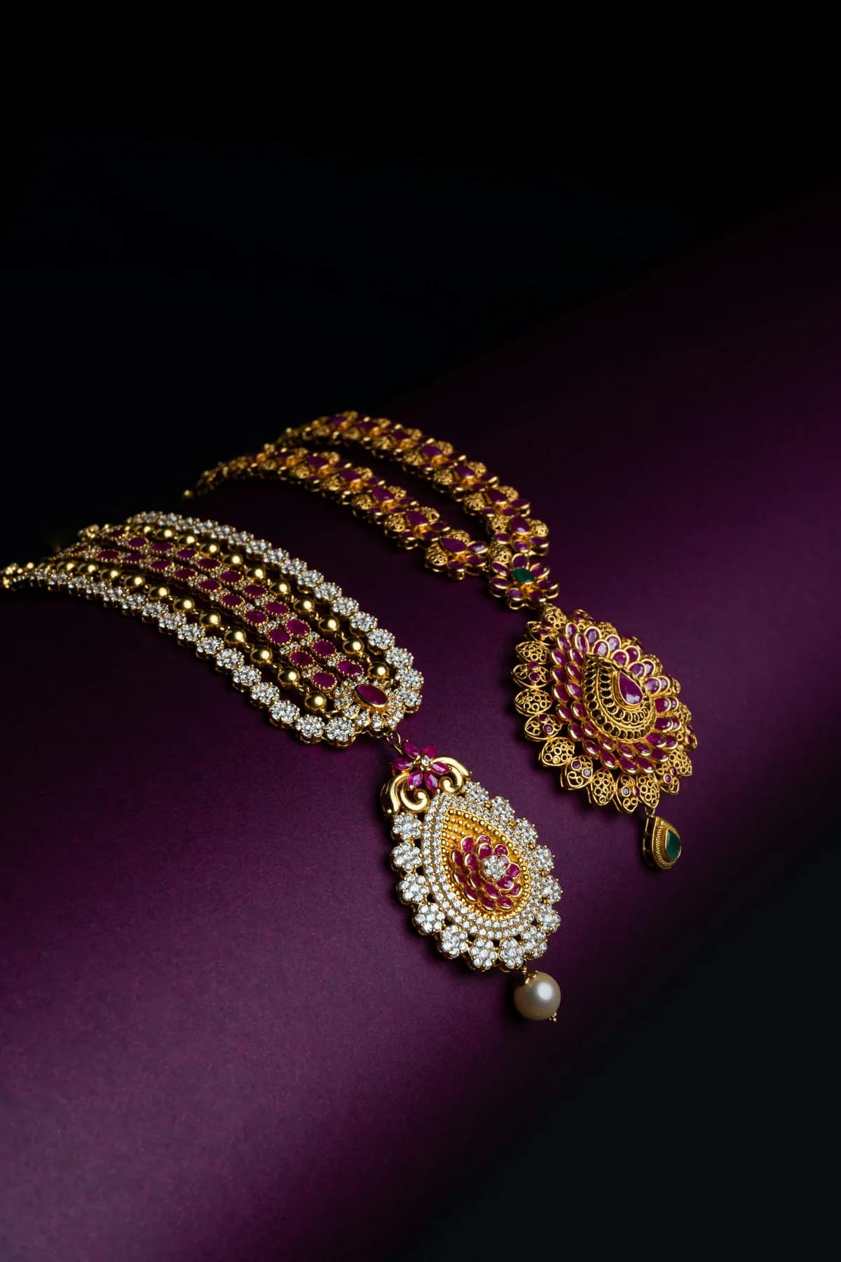 Two gold necklaces set with rubies and diamonds, laid across plum velvet